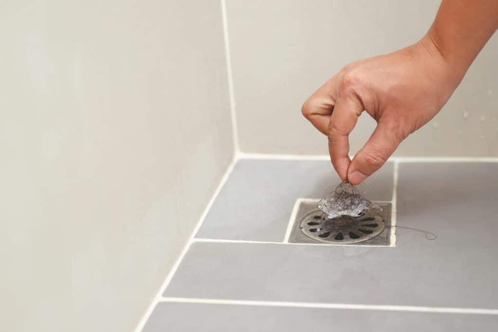 person unblocking blocked drain in shower